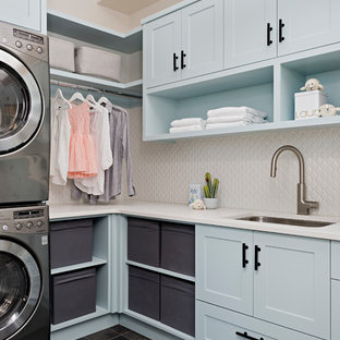 Imagen de cuarto de lavado en L, de estilo de casa de campo, con fregadero bajoencimera, armarios estilo shaker, puertas de armario azules, lavadora y secadora apiladas, suelo marrón y encimeras blancas