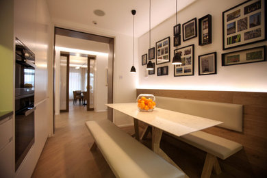 Medium sized contemporary l-shaped kitchen/diner in London with an integrated sink, flat-panel cabinets, white cabinets, quartz worktops, white splashback, stainless steel appliances, brown floors and white worktops.