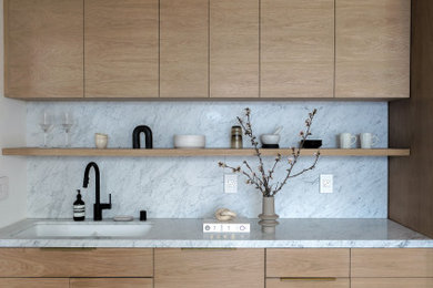 Small minimalist l-shaped medium tone wood floor and brown floor eat-in kitchen photo in San Francisco with a double-bowl sink, flat-panel cabinets, light wood cabinets, marble countertops, white backsplash, marble backsplash, stainless steel appliances, no island and white countertops