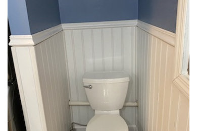 Small minimalist wood-look tile vinyl floor, brown floor and wainscoting powder room photo in Other with raised-panel cabinets, white cabinets, a two-piece toilet, blue walls, a drop-in sink, laminate countertops and a freestanding vanity