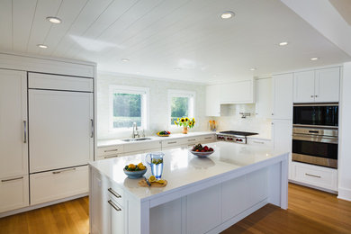 Example of a mid-sized trendy l-shaped kitchen design in New York with raised-panel cabinets, white cabinets, paneled appliances and an island