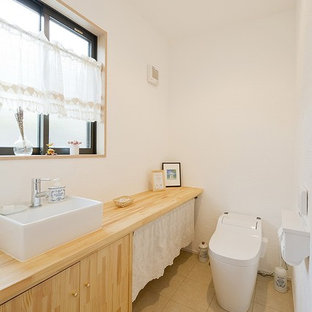 他の地域のカントリー風おしゃれなトイレ・洗面所 (フラットパネル扉のキャビネット、淡色木目調キャビネット、白い壁、ベッセル式洗面器、木製洗面台、ベージュの床、ベージュのカウンター) の写真