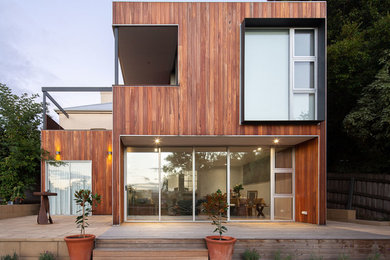 This is an example of a small modern two-storey brown house exterior in Other with wood siding, a flat roof and a metal roof.