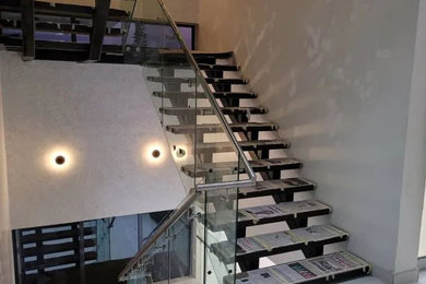 他の地域にあるお手頃価格の広いモダンスタイルのおしゃれな階段 (ガラスフェンス、レンガ壁) の写真