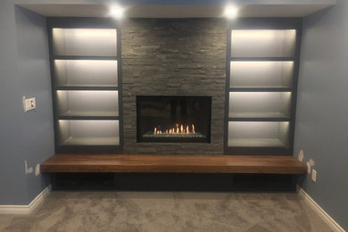 This is an example of a mid-sized transitional fully buried basement in Calgary with grey walls, carpet, a standard fireplace, a stone fireplace surround and beige floor.