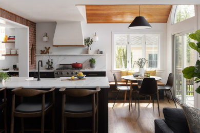 Ejemplo de cocina comedor abovedada clásica renovada grande con fregadero sobremueble, armarios estilo shaker, puertas de armario negras, encimera de cuarzo compacto, salpicadero blanco, puertas de cuarzo sintético, electrodomésticos de acero inoxidable, suelo de madera en tonos medios, península, suelo marrón y encimeras blancas