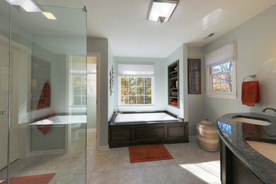 This is an example of a large contemporary master bathroom in Raleigh with open cabinets, dark wood cabinets, a drop-in tub, a corner shower, beige tile, porcelain tile, blue walls, porcelain floors, an undermount sink, granite benchtops, beige floor, a hinged shower door and grey benchtops.