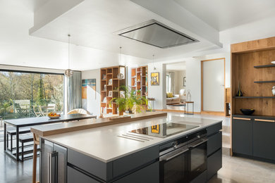 Inspiration for a large modern open plan kitchen in Gloucestershire with a built-in sink, flat-panel cabinets, grey cabinets, composite countertops, blue splashback, glass sheet splashback, black appliances, porcelain flooring, an island and brown floors.