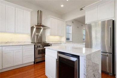 Eat-in kitchen - mid-sized transitional u-shaped light wood floor and brown floor eat-in kitchen idea in New Orleans with an undermount sink, shaker cabinets, white cabinets, marble countertops, white backsplash, ceramic backsplash, stainless steel appliances and an island