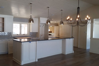 Inspiration for a large transitional l-shaped dark wood floor and brown floor eat-in kitchen remodel in Grand Rapids with shaker cabinets, white cabinets, solid surface countertops, gray backsplash, an island, matchstick tile backsplash and stainless steel appliances