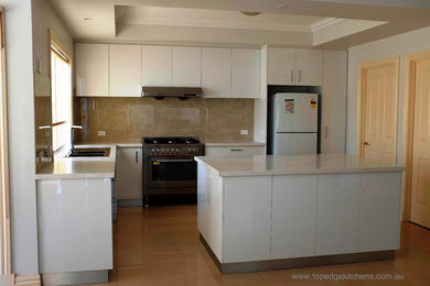 This is an example of a modern l-shaped eat-in kitchen in Melbourne with a double-bowl sink, white cabinets, quartzite benchtops, beige splashback, ceramic splashback, stainless steel appliances, ceramic floors, with island, beige floor and white benchtop.