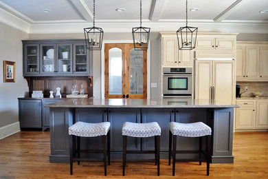 Elegant medium tone wood floor and orange floor kitchen photo in Other with raised-panel cabinets, beige cabinets, beige backsplash, stainless steel appliances and an island