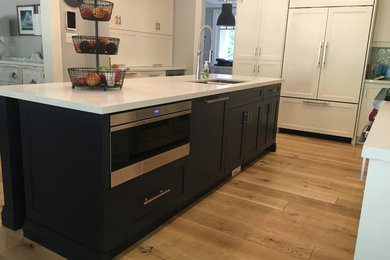 Eat-in kitchen - mid-sized transitional l-shaped medium tone wood floor eat-in kitchen idea in Toronto with a double-bowl sink, shaker cabinets, white cabinets, solid surface countertops, gray backsplash, stone tile backsplash, paneled appliances and an island