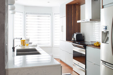 Inspiration for a contemporary galley kitchen remodel in Montreal with an undermount sink, white cabinets, quartz countertops, white backsplash, ceramic backsplash, stainless steel appliances and an island