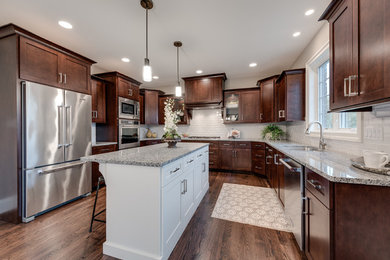 Photo of a large transitional u-shaped eat-in kitchen in Chicago with an undermount sink, flat-panel cabinets, dark wood cabinets, granite benchtops, white splashback, subway tile splashback, stainless steel appliances, dark hardwood floors, with island, brown floor and grey benchtop.