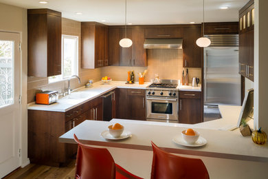 Inspiration for a mid-sized mid-century modern u-shaped medium tone wood floor and brown floor eat-in kitchen remodel in San Francisco with a double-bowl sink, flat-panel cabinets, dark wood cabinets, beige backsplash, ceramic backsplash, stainless steel appliances, a peninsula and white countertops