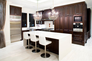 Example of a large minimalist l-shaped travertine floor open concept kitchen design in Vancouver with a farmhouse sink, raised-panel cabinets, dark wood cabinets, quartz countertops, white backsplash, ceramic backsplash, stainless steel appliances and an island