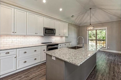 Open concept kitchen - transitional l-shaped gray floor open concept kitchen idea in Los Angeles with a farmhouse sink, shaker cabinets, white cabinets, granite countertops, white backsplash, subway tile backsplash, stainless steel appliances, an island and gray countertops