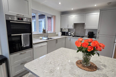 Design ideas for a medium sized contemporary l-shaped kitchen/diner in West Midlands with an integrated sink, shaker cabinets, grey cabinets, quartz worktops, multi-coloured splashback, stone slab splashback, black appliances, laminate floors, a breakfast bar, grey floors, multicoloured worktops and a coffered ceiling.