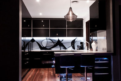 This is an example of a mid-sized modern u-shaped separate kitchen in Brisbane with an undermount sink, glass-front cabinets, black cabinets, quartz benchtops, multi-coloured splashback, glass sheet splashback, black appliances, medium hardwood floors and with island.