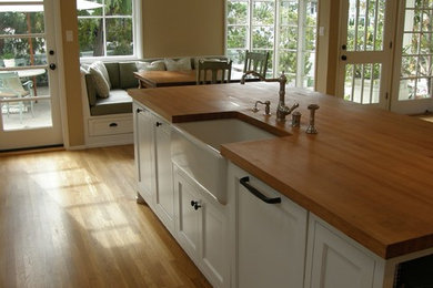 Kitchen - coastal light wood floor kitchen idea in Orange County with a farmhouse sink, recessed-panel cabinets, white cabinets, wood countertops, green backsplash, ceramic backsplash, white appliances and an island