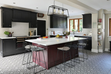 This is an example of a large classic l-shaped kitchen/diner in London with a belfast sink, shaker cabinets, black cabinets, quartz worktops, white splashback, engineered quartz splashback, black appliances, porcelain flooring, an island, multi-coloured floors and white worktops.