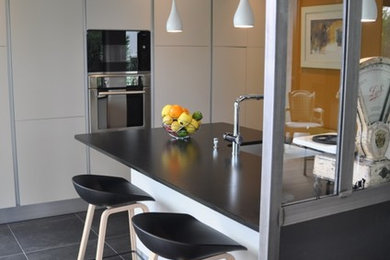 This is an example of a mid-sized contemporary single-wall open plan kitchen in Bordeaux with an undermount sink, beaded inset cabinets, stainless steel appliances, with island, grey floor and black benchtop.