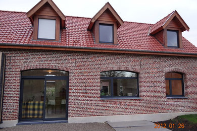 Aménagement d'une façade de maison rouge classique en brique de taille moyenne et à un étage avec un toit en tuile.