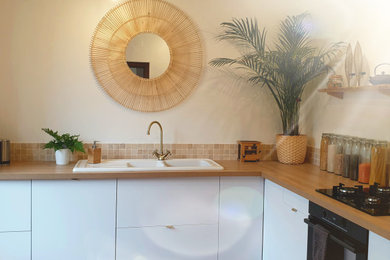Cette image montre une cuisine beige et blanche méditerranéenne avec un évier encastré, un plan de travail en bois, une crédence beige, une crédence en céramique, tomettes au sol, un sol marron et un plan de travail marron.