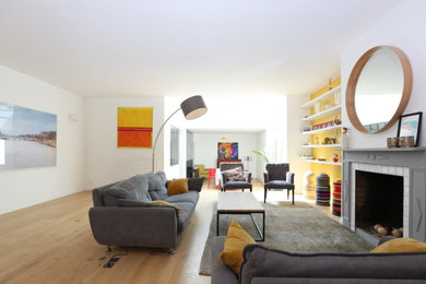 Cette image montre un grand salon blanc et bois design ouvert avec un mur jaune, parquet clair, une cheminée standard et un manteau de cheminée en plâtre.