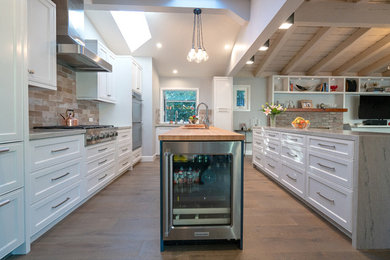 Photo of a small eclectic galley open plan kitchen in Los Angeles with an undermount sink, recessed-panel cabinets, white cabinets, quartzite benchtops, red splashback, ceramic splashback, stainless steel appliances, light hardwood floors, multiple islands, beige floor and white benchtop.