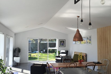 This is an example of a mid-sized industrial open concept family room in Christchurch with a music area, white walls, concrete floors and a freestanding tv.