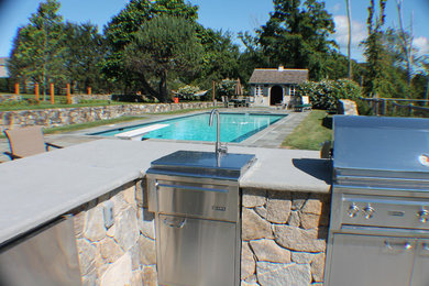 Example of a large transitional backyard stone patio kitchen design in New York with no cover