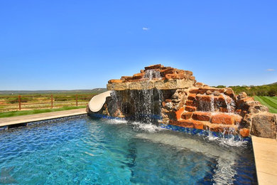 Expansive traditional backyard rectangular infinity pool in Dallas with a water slide and stamped concrete.