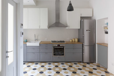 This is an example of a mid-sized scandinavian single-wall open plan kitchen in Milan with a single-bowl sink, grey cabinets, wood benchtops, ceramic splashback, stainless steel appliances, ceramic floors, multi-coloured floor, raised-panel cabinets and grey splashback.