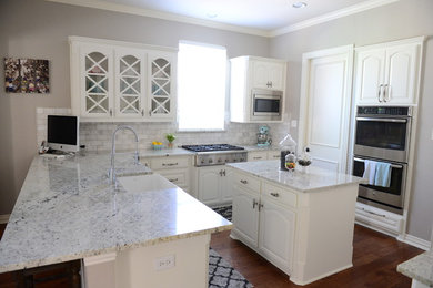 Open concept kitchen - large contemporary l-shaped medium tone wood floor open concept kitchen idea in Dallas with a farmhouse sink, raised-panel cabinets, white cabinets, marble countertops, white backsplash, stone tile backsplash, stainless steel appliances and an island