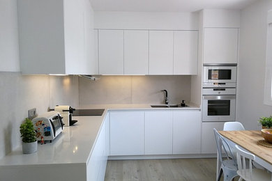 Photo of a large contemporary l-shaped eat-in kitchen in Other with an undermount sink, white cabinets, quartz benchtops, grey splashback, porcelain splashback, white appliances, light hardwood floors and white benchtop.