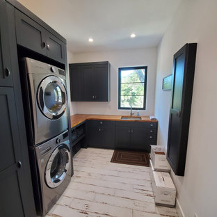 サンフランシスコの中サイズのカントリー風おしゃれな家事室 (アンダーカウンターシンク、シェーカースタイル扉のキャビネット、青いキャビネット、木材カウンター、白い壁、磁器タイルの床、上下配置の洗濯機・乾燥機、白い床、オレンジのキッチンカウンター) の写真