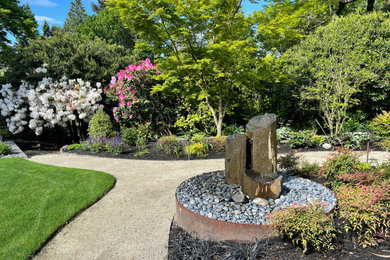 Diseño de jardín grande en patio delantero con jardín francés, fuente y granito descompuesto