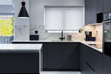 This is an example of a medium sized modern l-shaped kitchen/diner in London with a double-bowl sink, black cabinets, quartz worktops, white splashback, stone slab splashback, black appliances, porcelain flooring, an island, grey floors and white worktops.