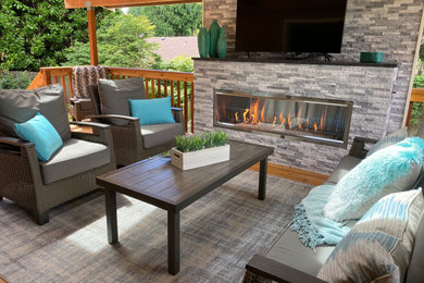 広いトランジショナルスタイルのおしゃれな裏庭のデッキ (屋外暖炉、張り出し屋根、木材の手すり) の写真