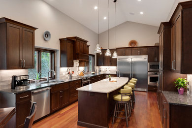 Inspiration for a large transitional u-shaped open plan kitchen in Minneapolis with an undermount sink, shaker cabinets, dark wood cabinets, quartz benchtops, white splashback, porcelain splashback, stainless steel appliances, medium hardwood floors, with island, brown floor and grey benchtop.