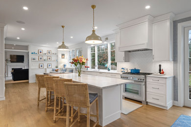 Kitchen - large transitional single-wall light wood floor and brown floor kitchen idea in Boston with an undermount sink, shaker cabinets, white cabinets, quartz countertops, white backsplash, ceramic backsplash, stainless steel appliances, an island and white countertops