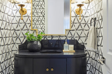 Inspiration for a mid-sized transitional powder room in Other with flat-panel cabinets, dark wood cabinets, a one-piece toilet, porcelain floors, an undermount sink, solid surface benchtops, beige floor, black benchtops, a freestanding vanity and wallpaper.