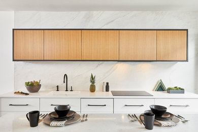 Photo of a mid-sized modern galley open plan kitchen in Philadelphia with an undermount sink, flat-panel cabinets, light wood cabinets, quartz benchtops, white splashback, marble splashback, panelled appliances, porcelain floors, with island, black floor and white benchtop.