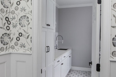 This is an example of a mid-sized eclectic galley dedicated laundry room in Philadelphia with an undermount sink, recessed-panel cabinets, white cabinets, grey walls, ceramic floors, multi-coloured floor, white benchtop, granite benchtops and a stacked washer and dryer.