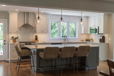 Mid-sized transitional galley eat-in kitchen in St Louis with an undermount sink, recessed-panel cabinets, white cabinets, white splashback, stainless steel appliances, medium hardwood floors, with island and brown floor.