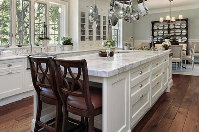Large transitional u-shaped medium tone wood floor and brown floor eat-in kitchen photo in Charlotte with a farmhouse sink, shaker cabinets, white cabinets, marble countertops, stainless steel appliances, an island and white countertops