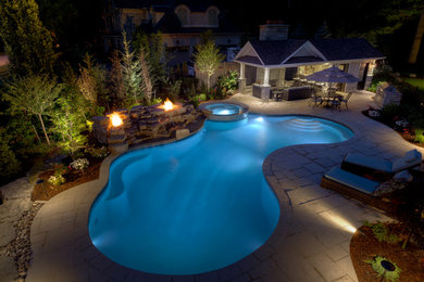 Photo of a large traditional backyard custom-shaped natural pool in Toronto with a hot tub.