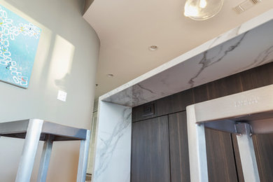 Inspiration for a small transitional galley medium tone wood floor and brown floor eat-in kitchen remodel in Atlanta with flat-panel cabinets, gray backsplash, stainless steel appliances, an island, an undermount sink, dark wood cabinets, glass tile backsplash and white countertops